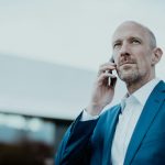 Confident businessman in blue suit talking on smartphone outdoors.